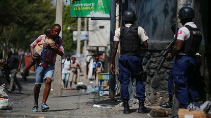 A parent carrying his child after picking him up from school, runs past police carrying out an operation against gangs in the Bel-Air area of Port-au-Prince, Haiti, on March 3, 2023.