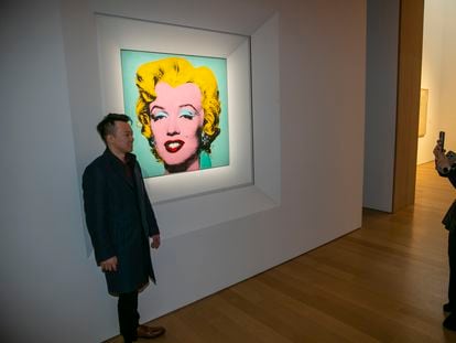 A visitor is photographed next to Warhol's painting, ‘Shot Sage Blue Marilyn.’