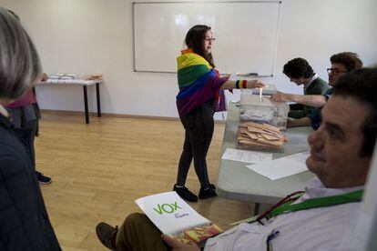 A woman draped in the LGBTQ flag votes at a polling station in Madrid as man holds Vox campaign material. Vox opposes same-sex marriage and wants to modify protections granted to the LGBTQ community.