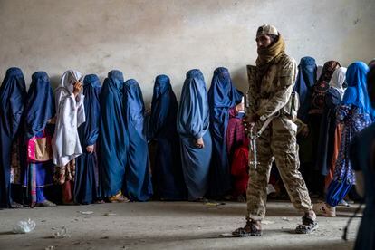 A Taliban fighter stands guard as women wait to receive food rations distributed by a humanitarian aid group, in Kabul, Afghanistan, on May 23, 2023.