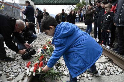 A boy lays flowers on the tracks at the railway station of Rapsani, north Greece, on March 5, 2023, during a commemorative gathering for the victims of a deadly train crash.