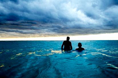 Two men take a dip in the ocean in Cuba, with storm clouds approaching.