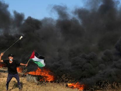A Palestinian protester uses sling shots to hurls stones while waves Palestinian flag as others burn tires during clashes with Israeli security forces along the frontier with Israel, east of Gaza City, Friday, Sept. 22, 2023.