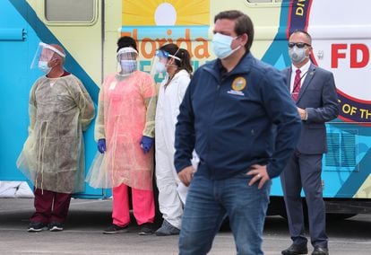 Health care workers and a security person look on as Florida Gov. Ron DeSantis waits to speak during a press conference at the Hard Rock Stadium testing site on May 6, 2020.