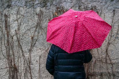 Sandra (not her real name) hides her face behind an umbrella on a rainy day in a town in the Madrid region.