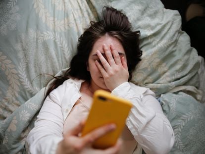 A woman in bed looks at her phone.