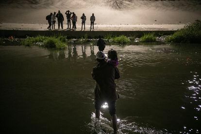 A man crosses the Rio Grande with a child in his arms, to surrender to the Border Patrol in Texas.