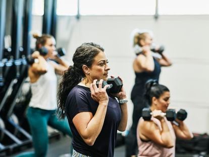 Woman doing dumbbell squats during fitness class in gym.
