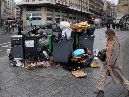 A woman walks past a pile of garbage cans Tuesday, March 7, 2023 in Paris.