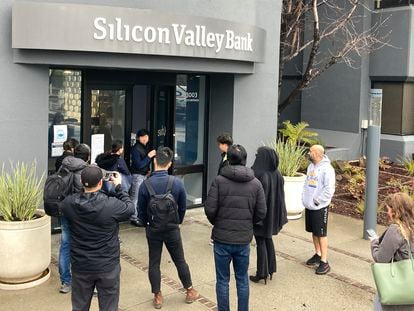A person from inside Silicon Valley Bank, middle rear, talks to people waiting outside of an entrance to Silicon Valley Bank in Santa Clara, Calif., Friday, March 10, 2023.