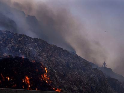 A person picks through trash for reusable items as a fire rages at the Bhalswa landfill in New Delhi, April 27, 2022.