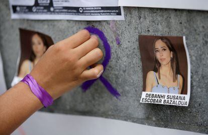 A woman attaches a purple ribbon on a wall with images of Debanhi Escobar, in San Nicolás de los Garza, Mexico.