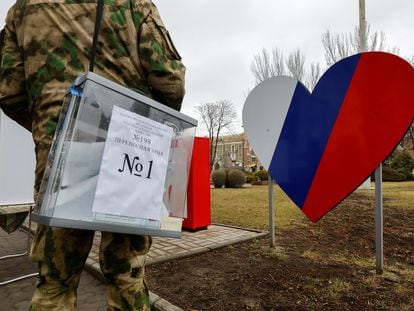 A military member of the electoral commission of occupied Donetsk carries a ballot box at a voting point located in the middle of the street.