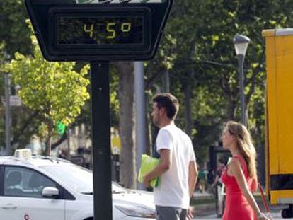 A couple walks past a thermometer on a street in Zaragoza.