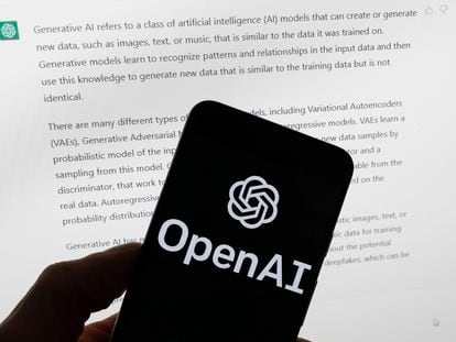 The OpenAI logo is seen on a mobile phone in front of a computer screen displaying output from ChatGPT, on March 21, 2023, in Boston.