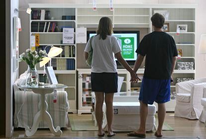 A couple holds hands in front of an empty living room at a Chicago IKEA.