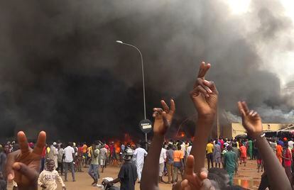 With the headquarters of the ruling party burning in the back, supporters of mutinous soldiers demonstrate in Niamey, Niger, Thursday, July 27 2023