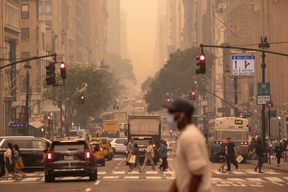 A man wears a mask as he crosses an intersection in a haze-filled sky of Manhattan, New York