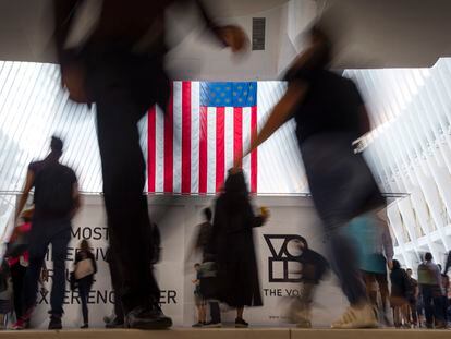 People walk past an American flag inside the Oculus, part of the World Trade Center transportation hub, at the start of a work day in New York, in 2019.