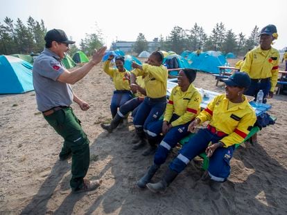 Frank McKay, left, a veteran wildfire fighter and liaison officer with the Northwest Territories Government Department of Environment and Climate Change, entertains South African firefighters with a Dene handgame at Yellowknife Airport in Yellowknife, Canada, Tuesday, Aug. 15, 2023. The city of Yellowknife, the territorial capital, declared a local state of emergency Monday night, citing an imminent wildfire threat. (Bill Braden/The Canadian Press via AP)