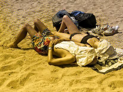 A couple sunbathes on a beach in Barcelona, Spain.