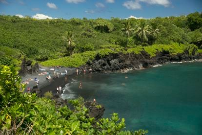 People spend time on the black sand beach at Waianapanapa State Park in Hana, Hawaii