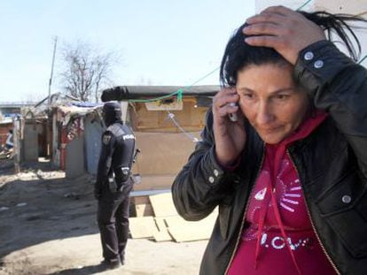 A woman speaks on the phone as a nearby police officer observes the demolition of shacks in El Gallinero.