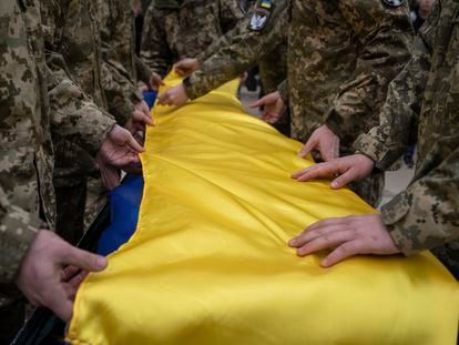 Ukrainian servicemen fold the national flag over the coffin of their comrade Andrii Neshodovskiy during the funeral ceremony in Kyiv, Ukraine, Saturday, March 25, 2023.