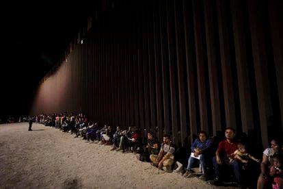 Migrants wait along the border wall after crossing from Mexico to the US near Yuma (Arizona).