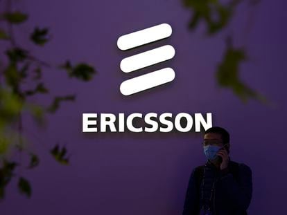 A man wearing a face mask talks on his smartphone near a booth from Swedish technology firm Ericsson at the PT Expo in Beijing, Wednesday, Oct. 14, 2020.