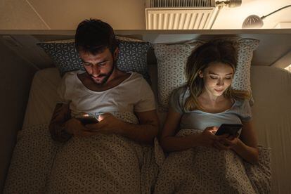 A couple looking at their mobile phones in bed.