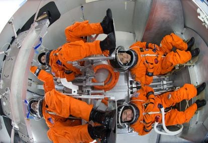 Cuatro ingenieros con trajes espaciales se sientan en una répilca de la cápsula Orion, con el comandante y el piloto en la parte izquierda.