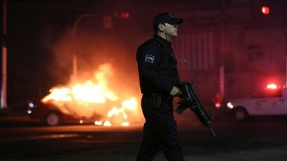 A police officer stands near a vehicle set on fire by members of Jalisco New Generation Cartel.