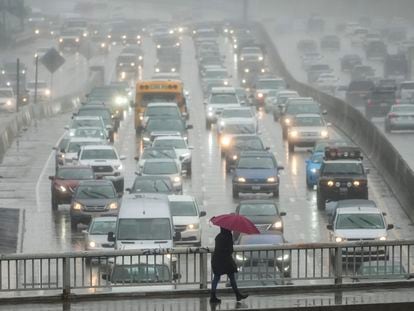 A pedestrian walks with an umbrella as motorists drive through rain along the 110 Freeway in the Hollywood section of Los Angeles, Friday, March 10, 2023. Evacuations were ordered Friday in Northern California after a new atmospheric river brought heavy rain, thunderstorms and strong winds, swelling rivers and creeks and flooding several major highways during the morning commute.