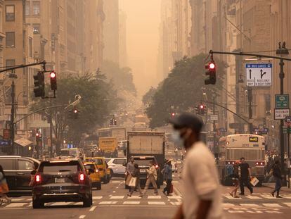 A man wears a mask as he crosses an intersection in a haze-filled sky of Manhattan, New York, on June 7, 2023.