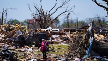 A woman walks near an uprooted tree, a flipped vehicle and debris from homes damaged by a tornado, March 27, 2023, in Rolling Fork, Mississippi.