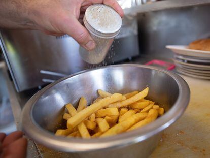 A man pours salt into a bowl of potato chips.