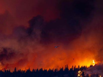 A helicopter battles the McDougall Creek wildfire as it burns in the hills West Kelowna, British Columbia, Canada, on August 17, 2023, as seen from Kelowna.