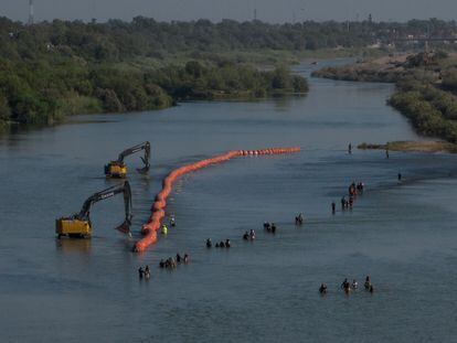 A group of migrants passes by the 'floating wall' during its construction on the Rio Grande, near Eagle Pass.
