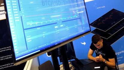 A man works beneath a display showing the market price of bitcoin.