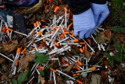 A volunteer cleans up needles used for drug injection that were found at a homeless encampment, in 2017.