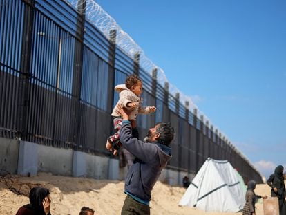 Naser Abu Mustafa, a Palestinian displaced by Israeli attacks, holds his granddaughter in his arms next to the border fence between Gaza and Egypt.
