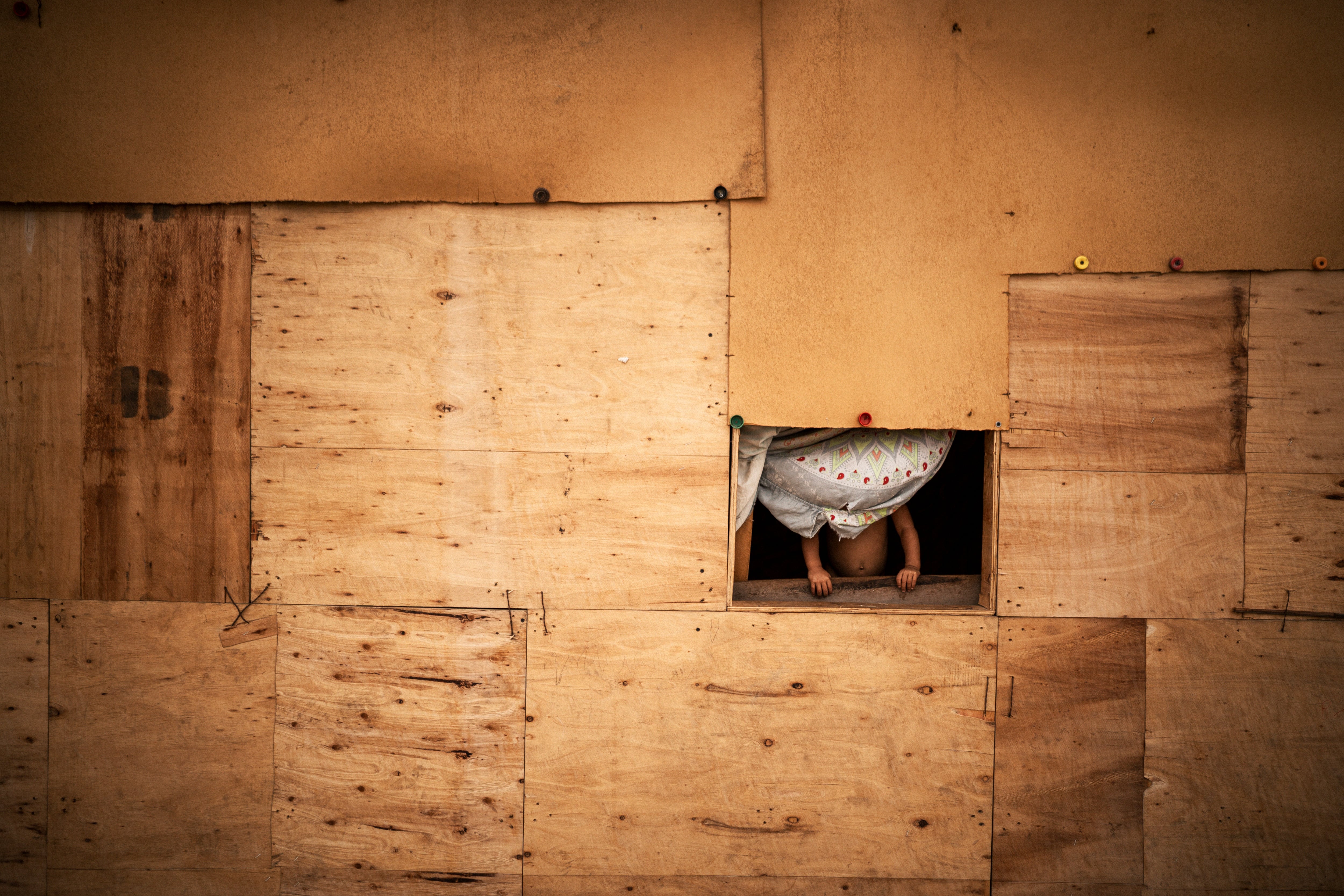 A girl looks out the window of a makeshift wooden house in La Pista, April 23, 2025.