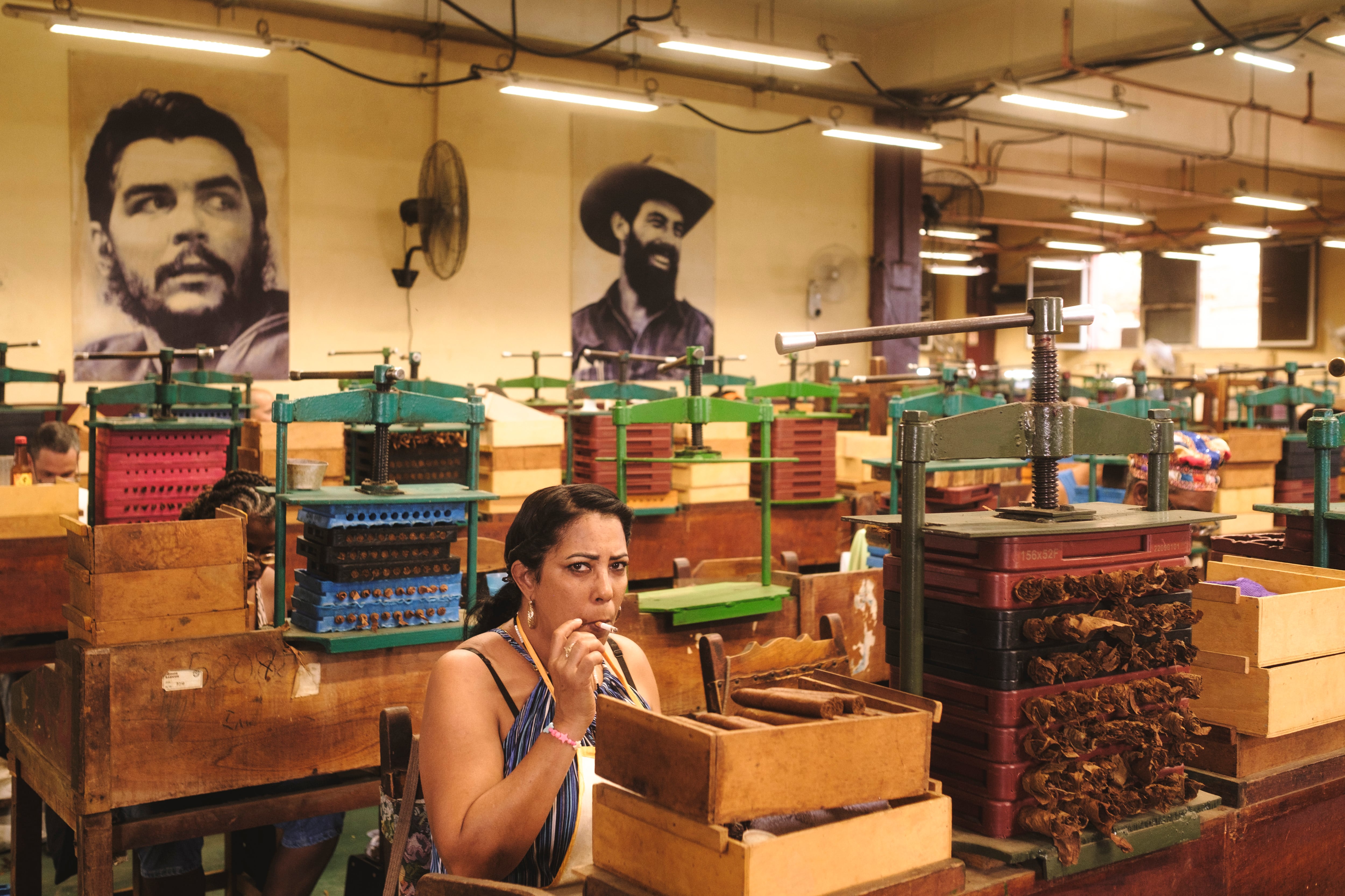 A woman smokes a Habano while working at La Corona Cigar Factory.