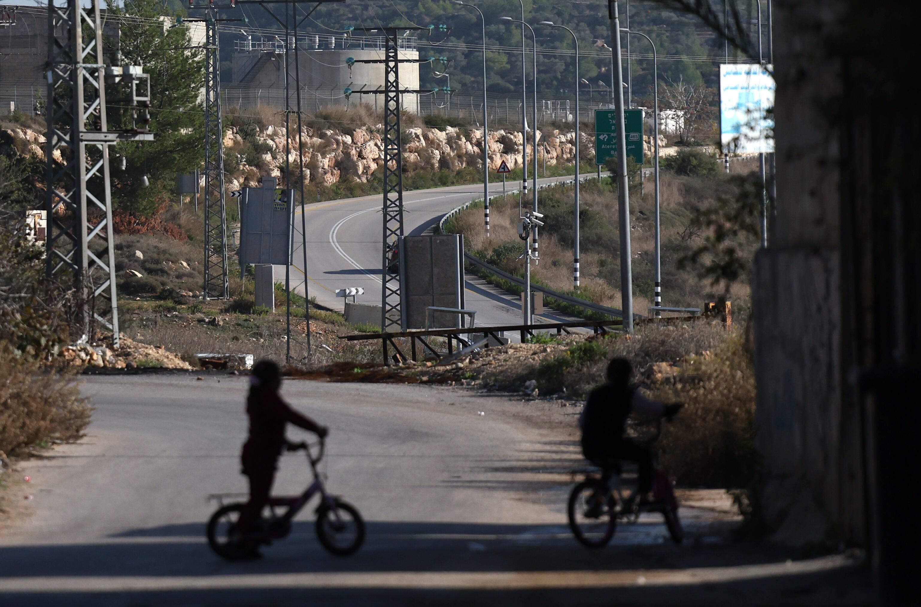 Two children look out over the road leading to the Israeli settlement of Ateret, where Palestinians are prohibited from traveling, in December 2023.