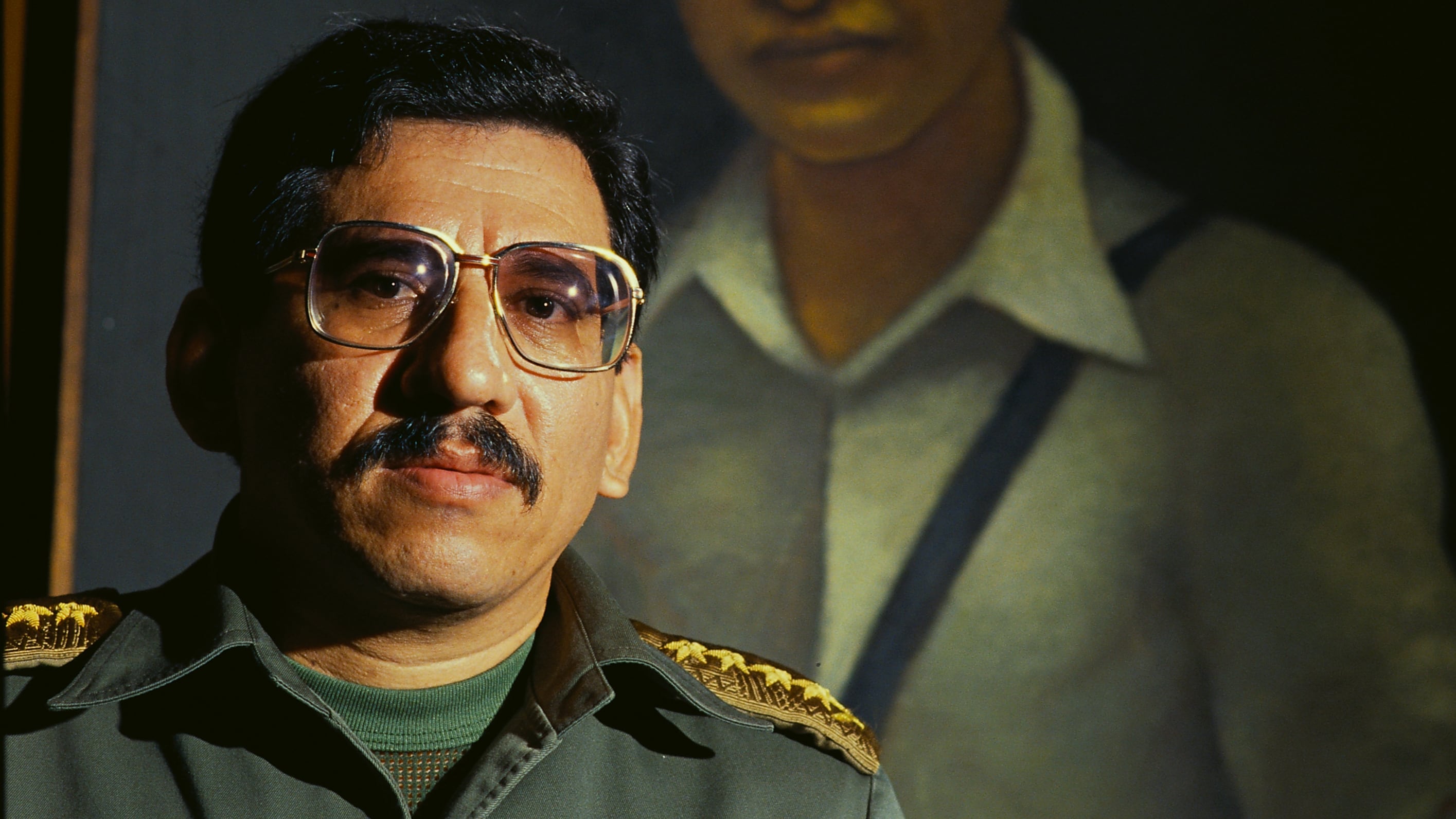 Humberto Ortega, standing under a portrait of César Augusto Sandino, in an archive image.