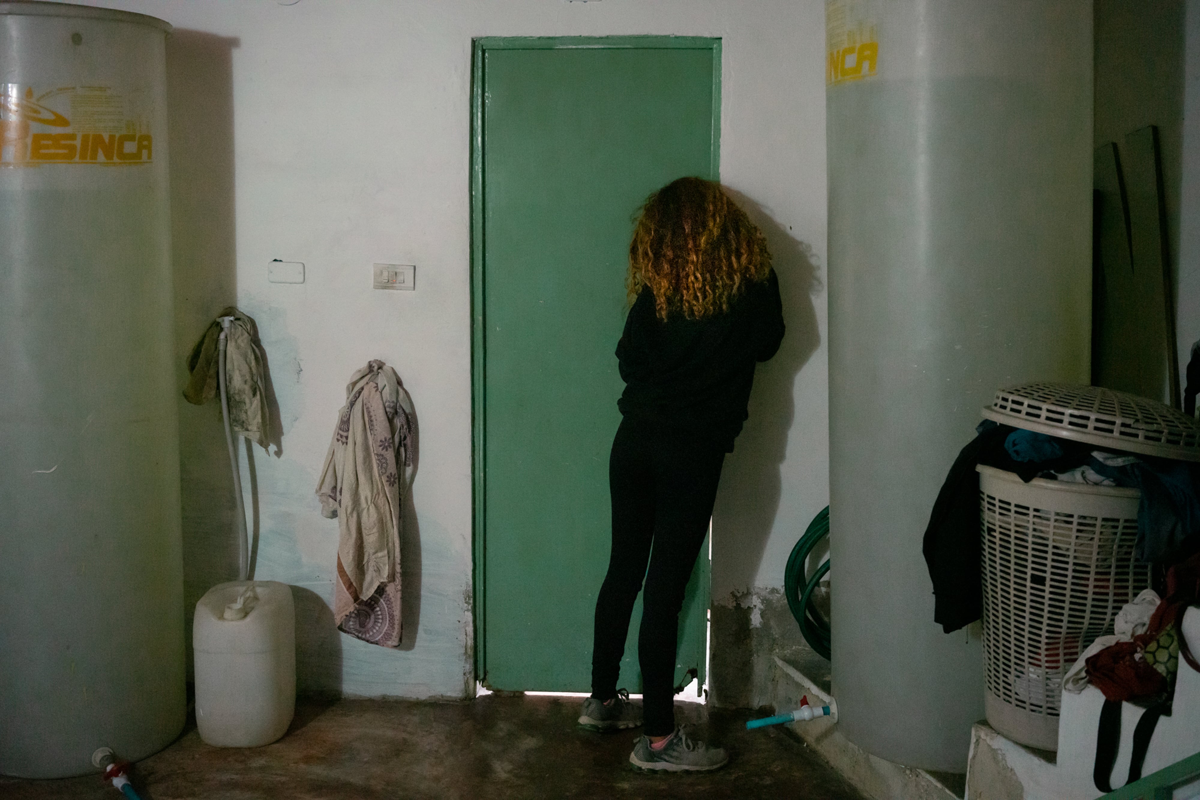 A companion asks a woman undergoing a medical abortion if she can enter the bathroom, in order to hold her hair and body while she vomits and sits on the toilet. Photo taken in a house located in a working-class neighborhood of Caracas, Venezuela, on August 25, 2022. Near this house, police forces are stopping everyone entering the neighborhood at a makeshift checkpoint.