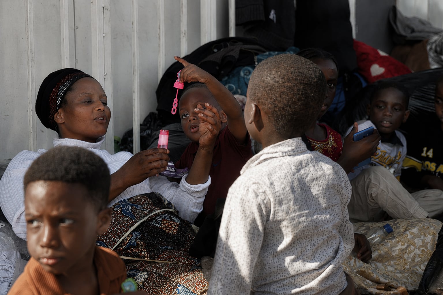 A woman and kids play to while away the time on the sidewalk where they live after being expelled from their homes in  Durban, on July 5, 2026.