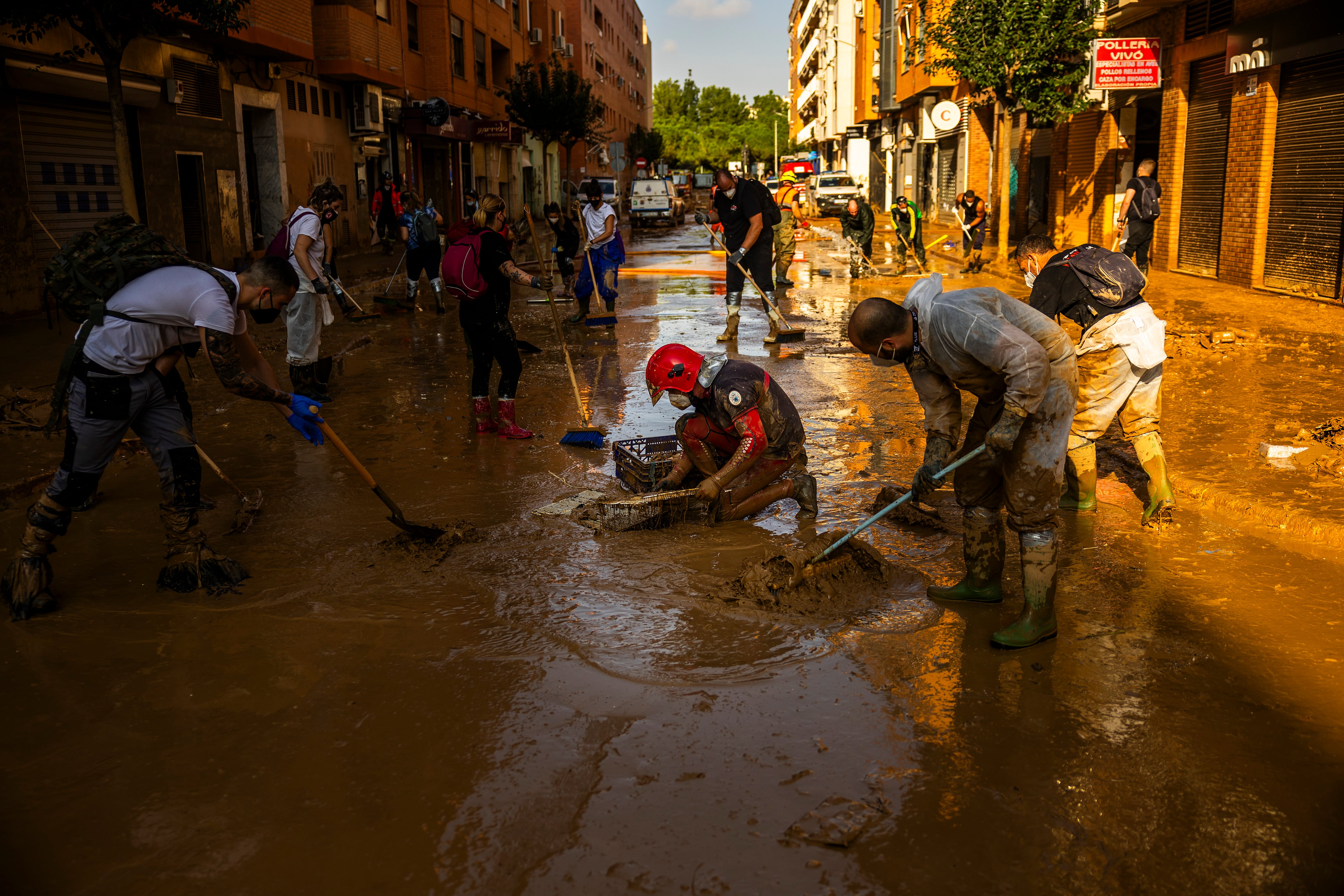 A firefighter and a group of volunteers pump out water and mud from a sewer near Blasco Ibáñez Avenue, in Catarroja.