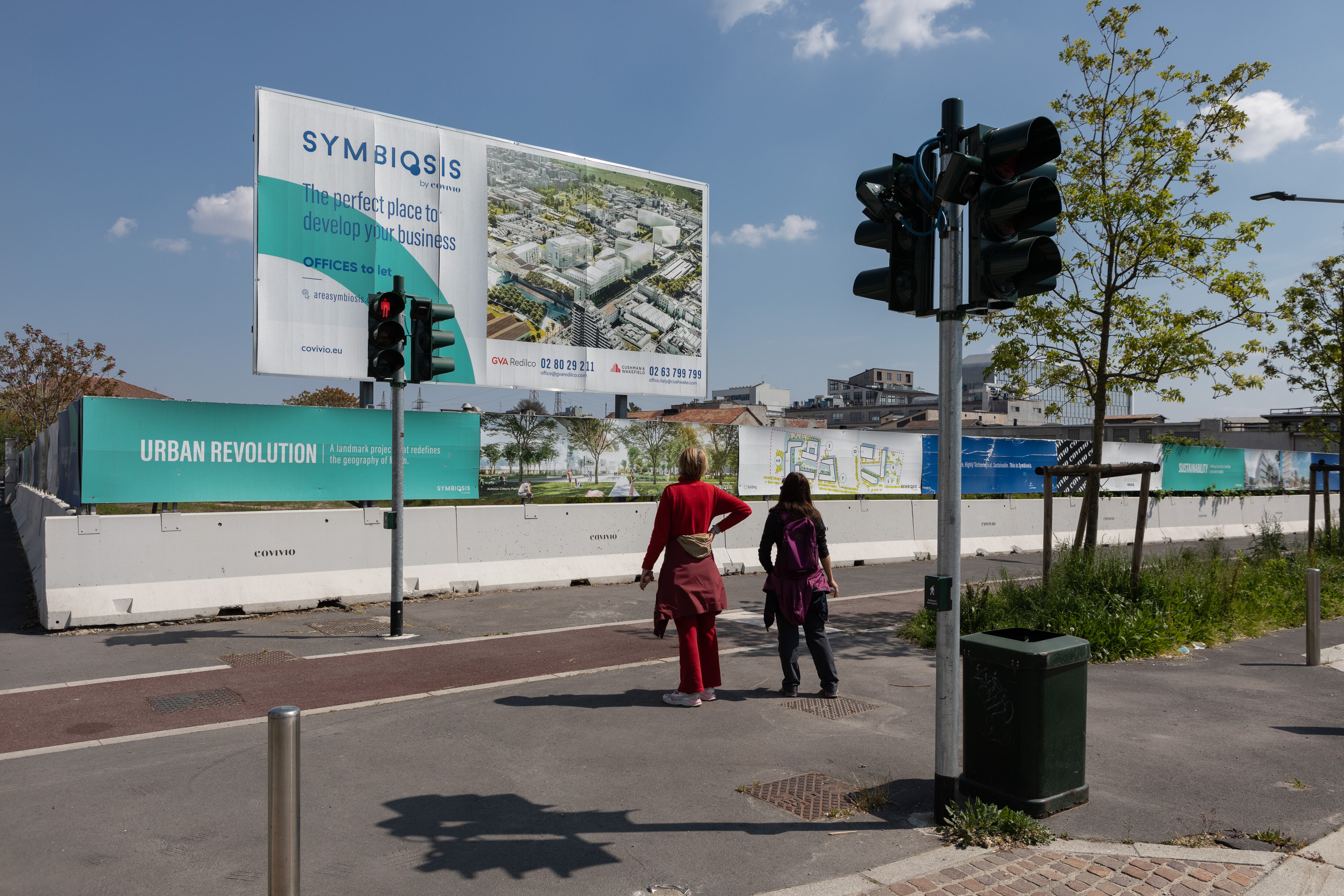 Two women look at a billboard that displays an AI generated image of the planned Symbiosis housing complex in Milan.